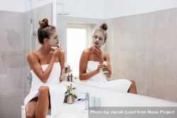 Young woman applying facial mud clay mask to her face in bathroom. 0PkV7b