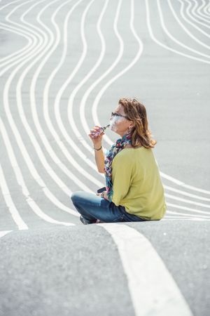 Modern relaxed woman vaping while sitting on marked road