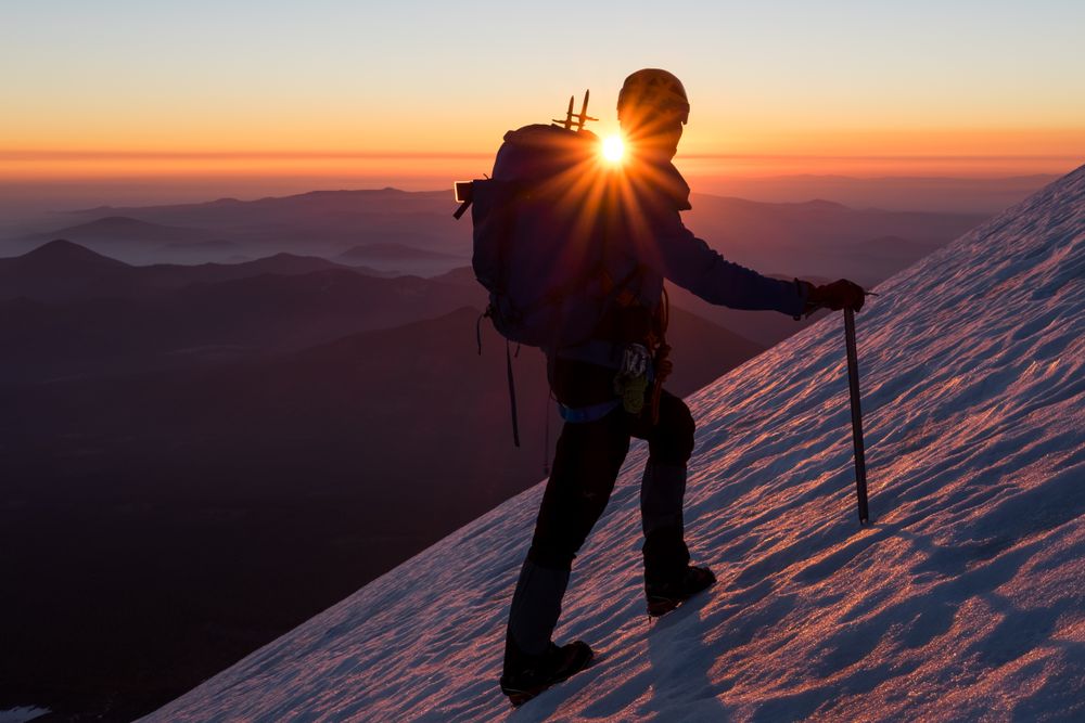 Silhouette of person climbing snow covered steep during sunset