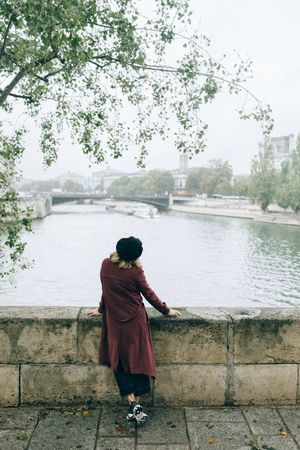 Woman in red jacket standing on concrete bridge over body of water