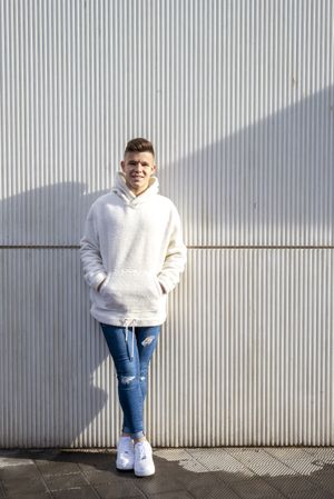 Portrait of young adult with hands in pocket leaning on wall outside