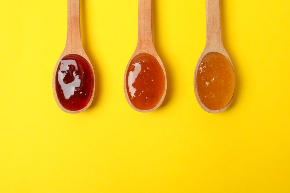 Spoons with jam on yellow background, top view