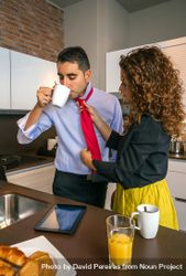 Curly haired woman adjusting tie of man while having fast breakfast before work 5kqz6b