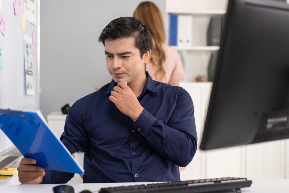 Man sitting at his office desk reviewing notes on clipboard