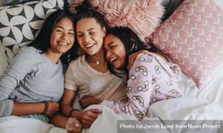 Group of girls laughing and having fun while lying on bed together during sleepover 5rqOp0