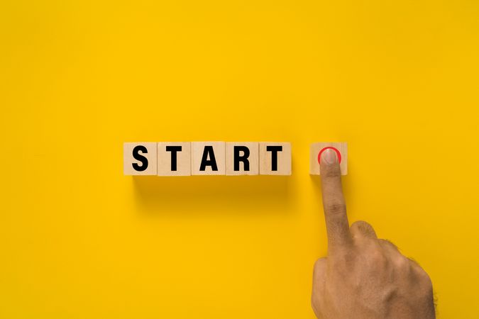 male hand press start button on wooden blocks isolated on yellow background