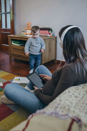Pregnant using the tablet while her son is playing