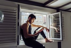 Young male sitting on window and reading book