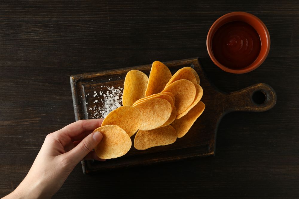 Potato chips on a wooden board with salt on a dark background