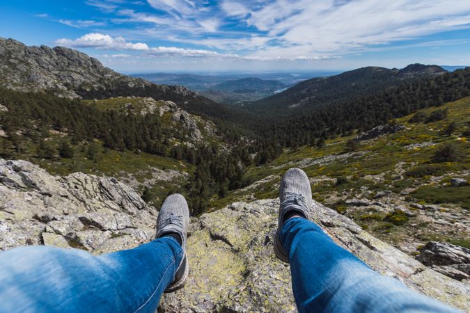 Person sitting dangling legs on stone above mountain valley