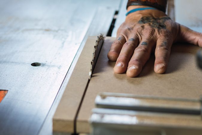 Crop male carpenter cutting wood with circular saw