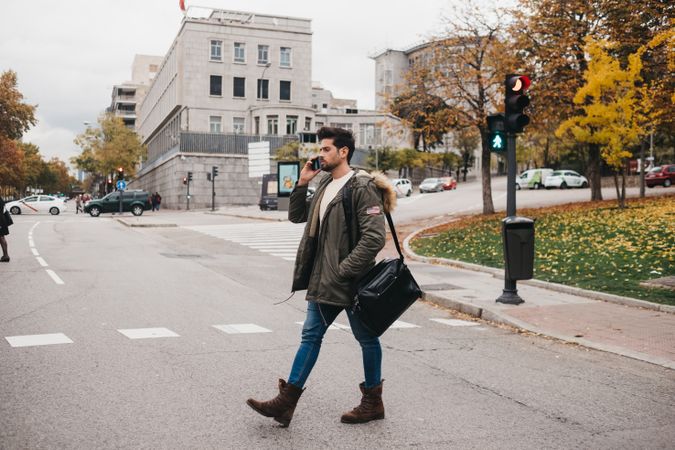 Busy male with smartphone crossing road
