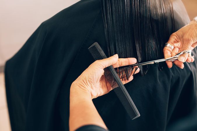 Skilled hairdresser trimming client’s long straight hair