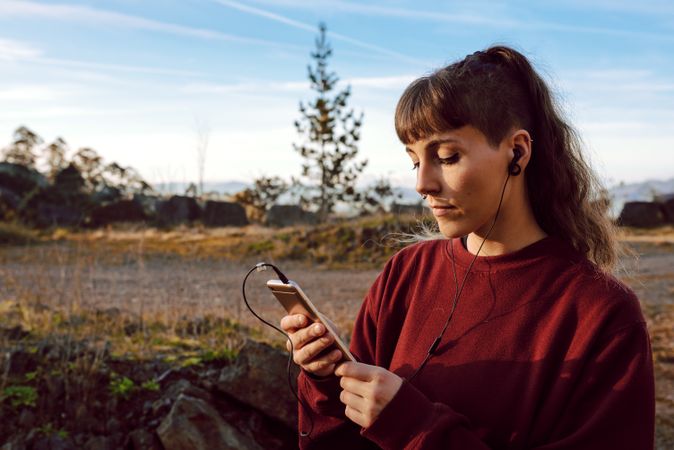 Young woman with piercing listening music on smartphone on hill