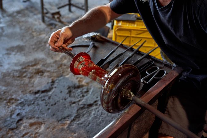 Anonymous worker glassblowing bottle in workshop
