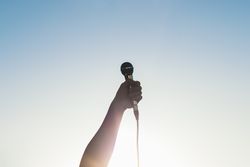 man hand holding a microphone outdoors with sunlight reflects