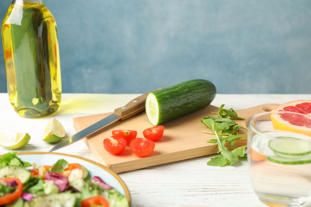 Salad ingredients, knife and oil on wooden background, space for text