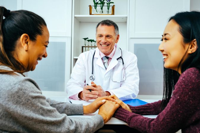 Smiling doctor sharing news with two happy patients in medical office