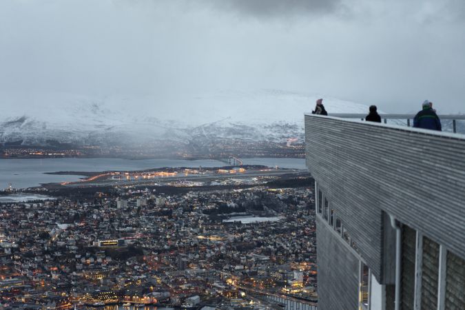 Tourists enjoying wonderful view of city against snowy mountain standing on viewpoint in evening