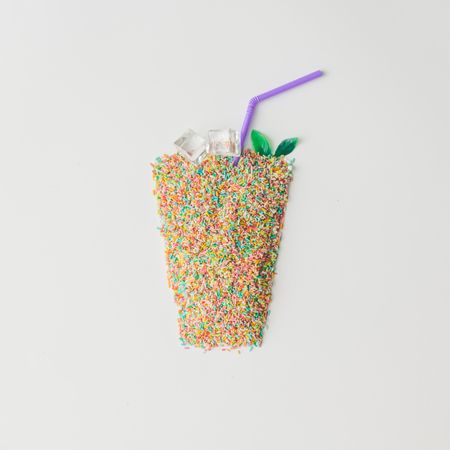 Glass made of colorful cake sprinkles with straw and ice
