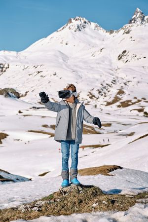Anonymous boy exploring VR goggles in snowy mountains
