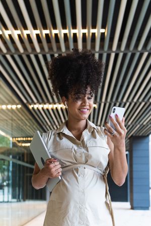 Smiling Black pregnant woman using smartphone and wireless earphones