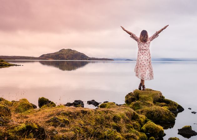Side view of traveller woman standing on lake shore and pulling hand up in Iceland