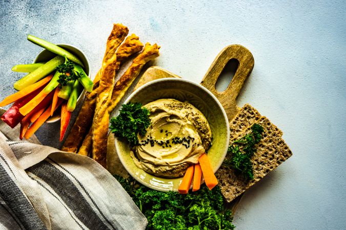 Top view of traditional hummus dip in bowl on board served with veggies and rye crackers