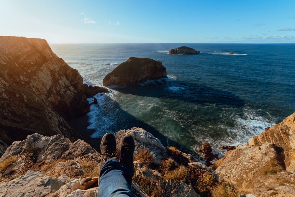 Person sitting on cliff near water