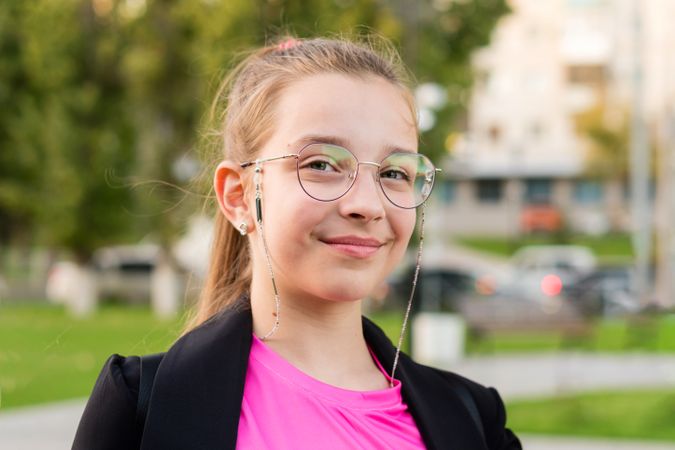 Girl wearing glasses smiles outdoors in park.
