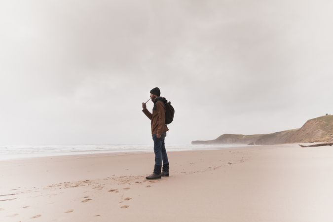 Man smoking pipe on sand shore near water