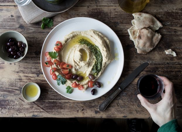 Crop hand dipping flatbread into hummus pesto with tomatoes and beans