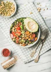 Healthy vegan lunch bowl with avocado, sprouted grains, vegetables, paprika, on checkered napkin
