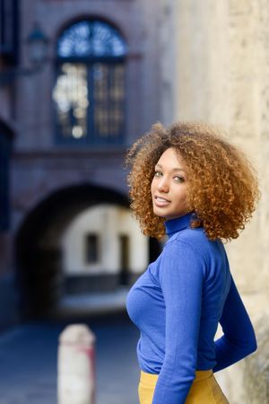 Woman with curly hair looking around in front of European city street