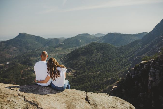Happy couple sitting at mountain cliff