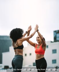 Side view of two fitness women giving high five standing on rooftop 5kWaD5