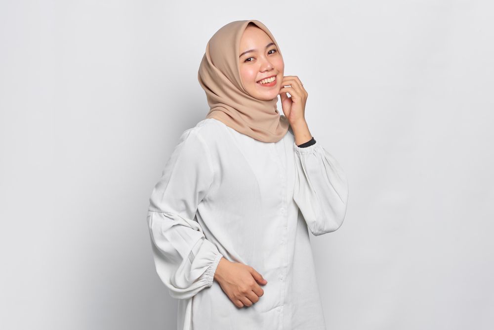 Side view of smiling Asian female in headscarf with hand on chin