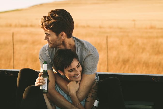 Man and woman holding each other while enjoying a bottled beer on road trip