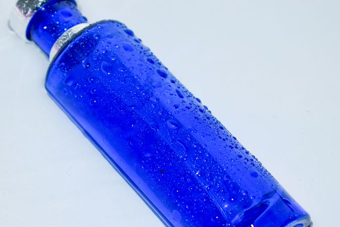Blue perfume bottle with water droplets laying on light background