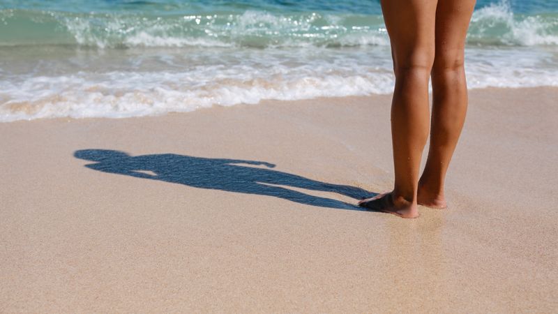 Feet of a woman with shadow on the sea shore