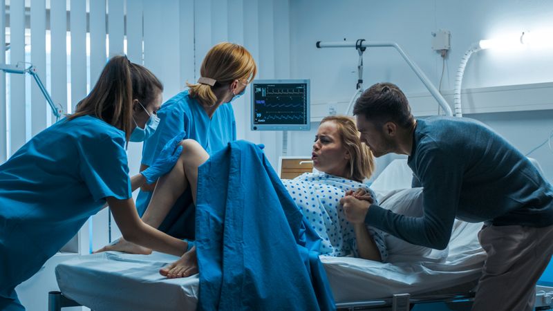 In the Hospital Woman in Labor Pushes to Give Birth, Obstetricians Assisting, Help Spreading Her Legs