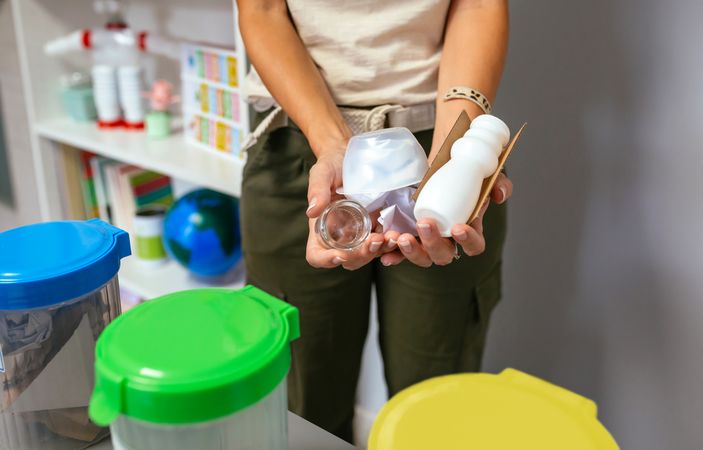 Female teacher holding waste to recycle with selective trash bins in foreground