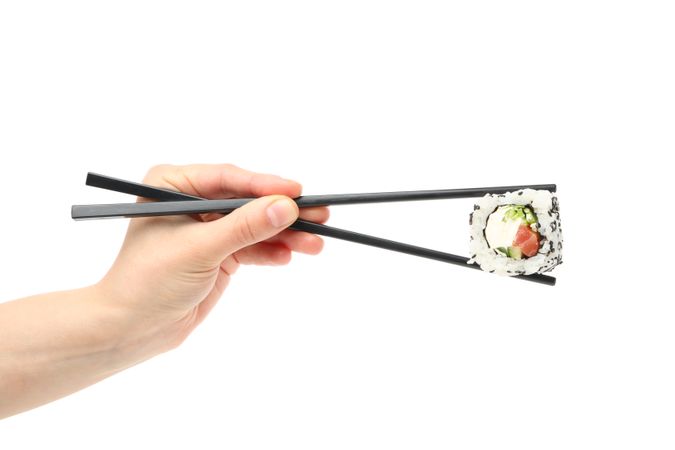Female hand with chopsticks holds sushi roll, isolated on plain background