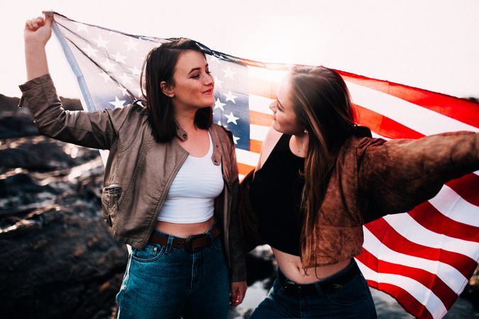 Two young women smiling at each other while holding the American flag above their heads