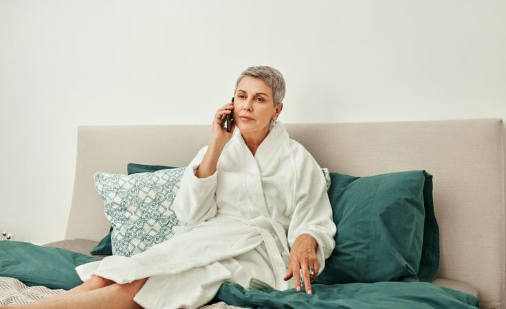Mature woman taking a call while relaxing on a green bed