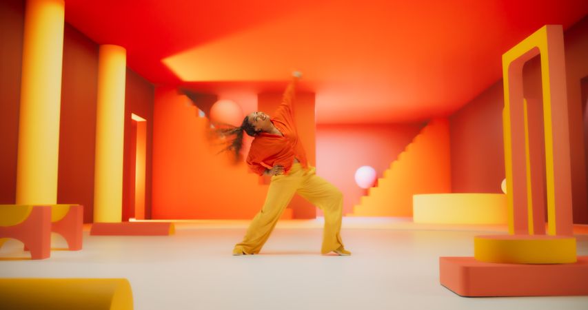 Black Woman in Bright Outfit Dancing Energetically in Geometric Abstract Orange, Yellow Environment. Creative Young Female Performing Modern Dance Choreography in a Studio