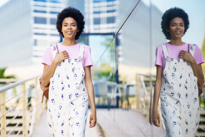 Smiling female in floral overalls walking outside past corporate building