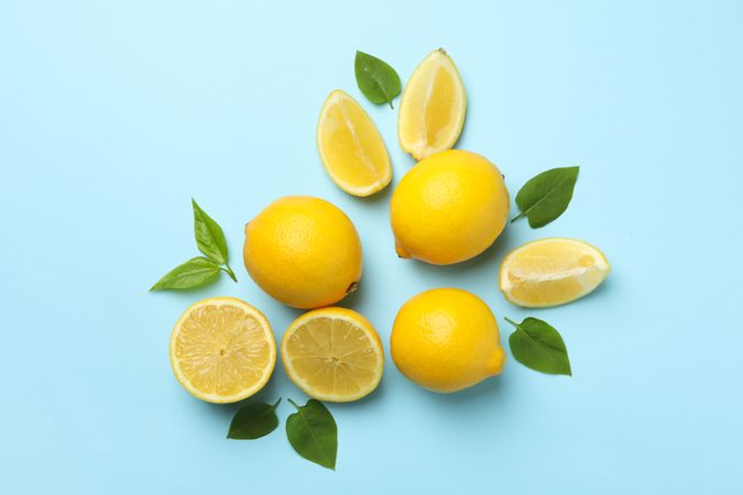 Fresh lemons with leaves on blue background, top view. Ripe fruit