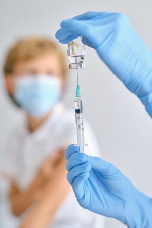 Crop nurse filling syringe with vaccine against patient in hospital