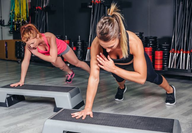 Two women working out upper body on step in fitness class